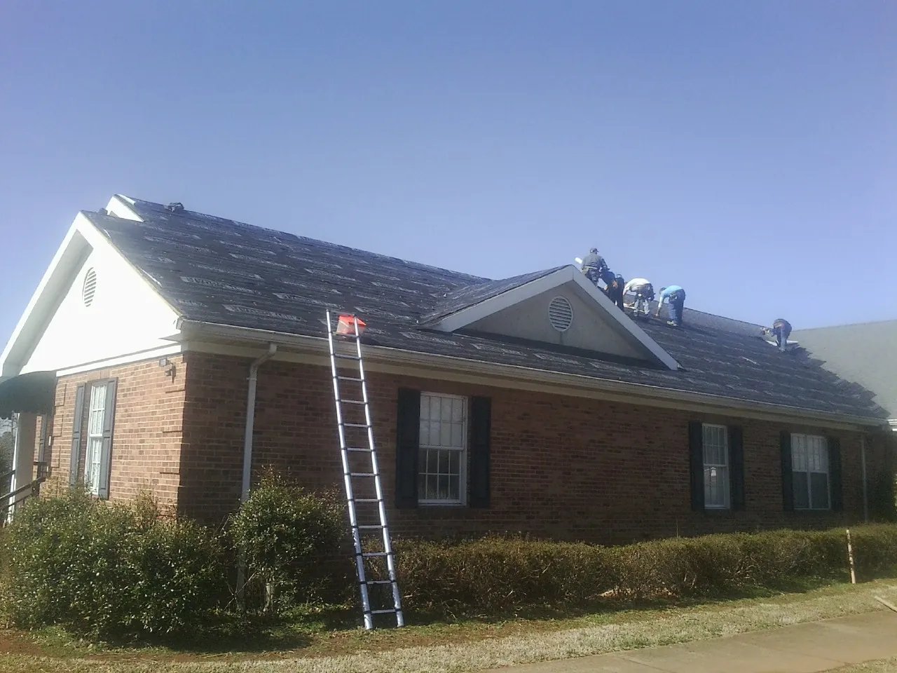 Crew tearing shingles off a brick ranch roof with a ladder set — Emergency Roof Repair work by our crew in Elkton